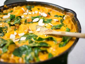 Close up of butternut squash and chickpea curry in black skillet with wooden spoon