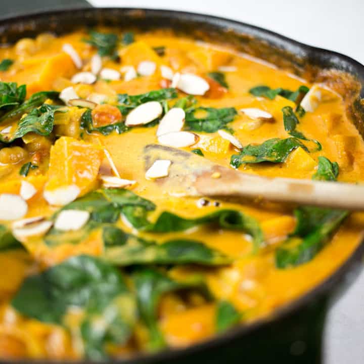 Close up of butternut squash and chickpea curry in black skillet with wooden spoon