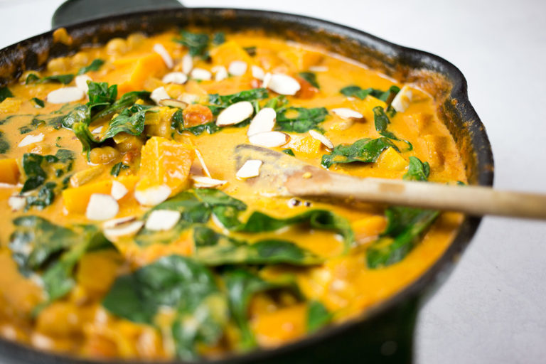 Close up of butternut squash and chickpea curry in black skillet with wooden spoon