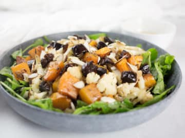 Close up of pumpkin and cauliflower salad in blue bowl with white background.