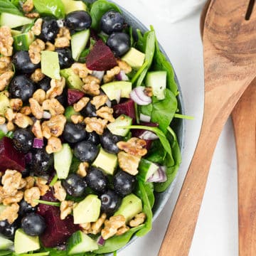 Spinach and Blueberry Salad in bowl with serving spoons to the right.