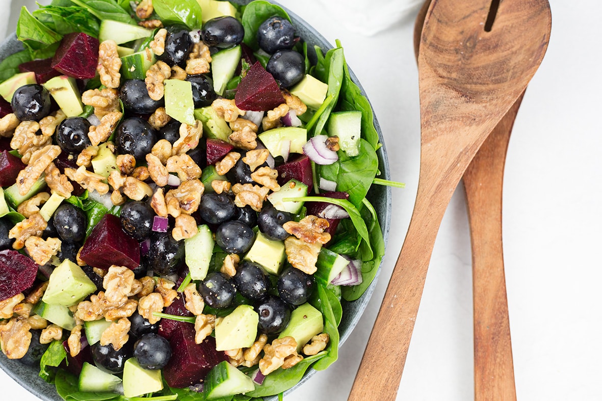 Spinach and Blueberry Salad in bowl with serving spoons to the right.