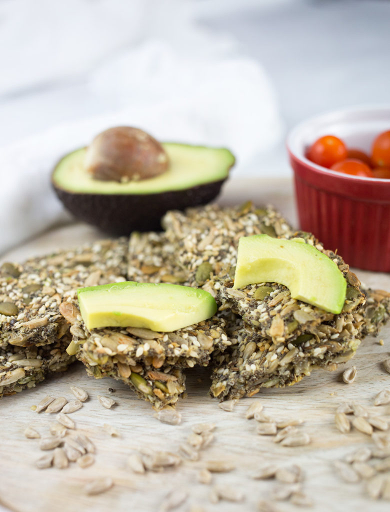 Close up off seed crackers on chopping board with sliced avocado on top.