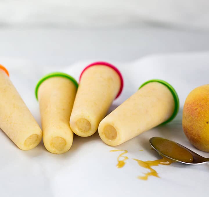Four popsicles on white background with honey drizzles and peach in the background.