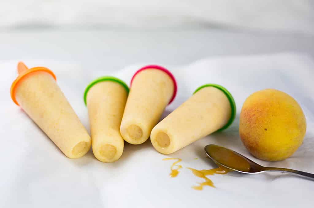 Four popsicles on white background with honey drizzles and peach in the background.
