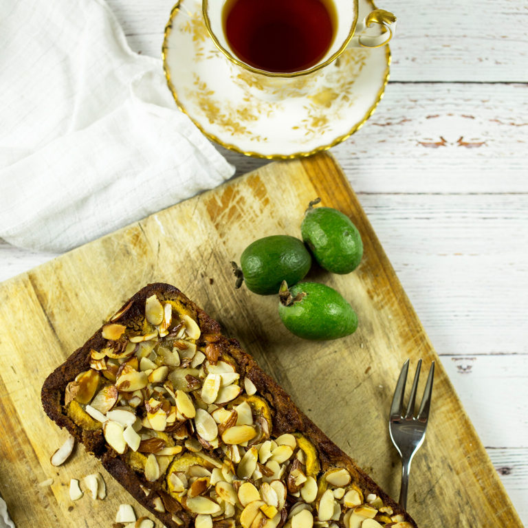 Birdseye view of feijoa and banana loaf on chopping board with cup of tea in background.
