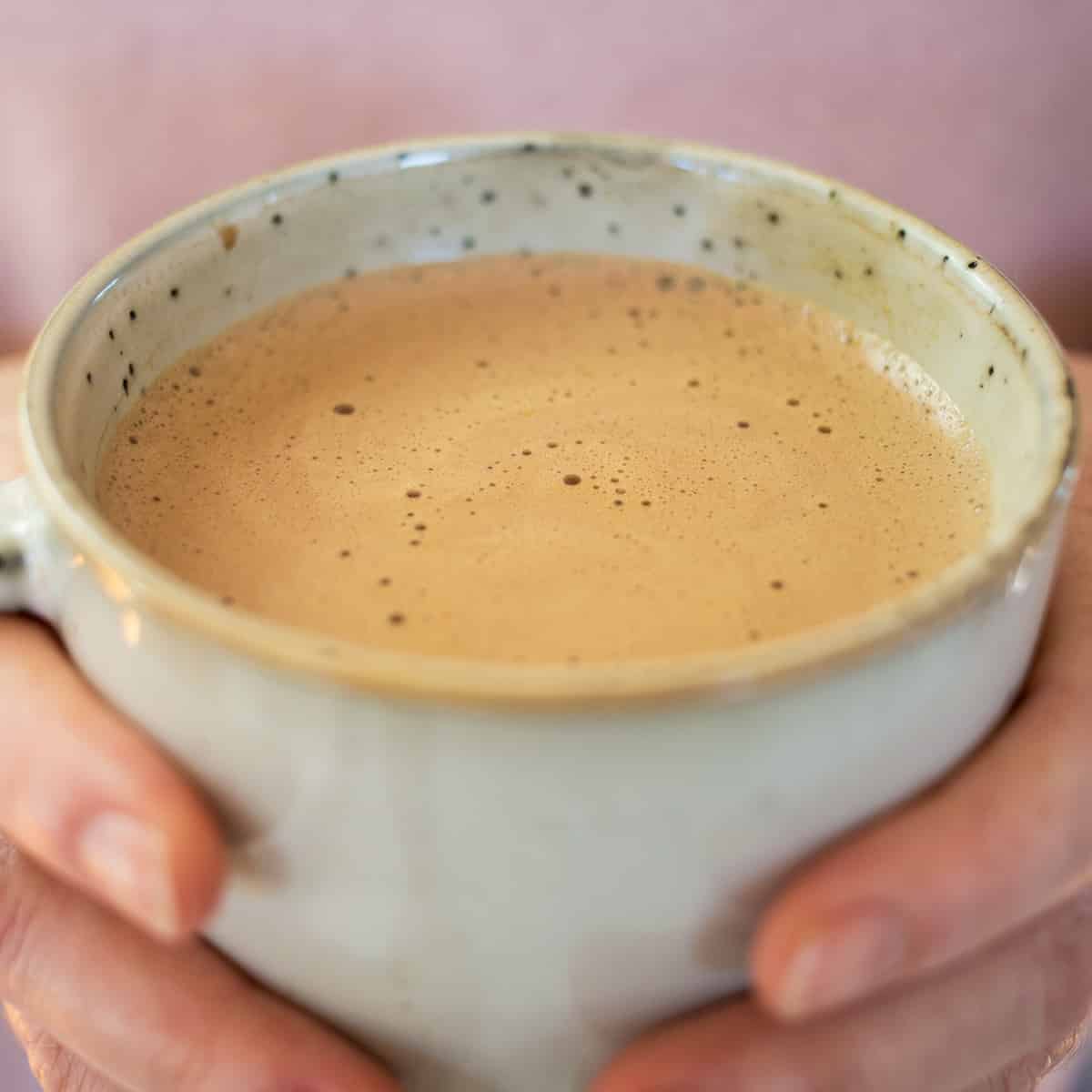 Close up of hands holding Paleo hot chocolate with pink background.