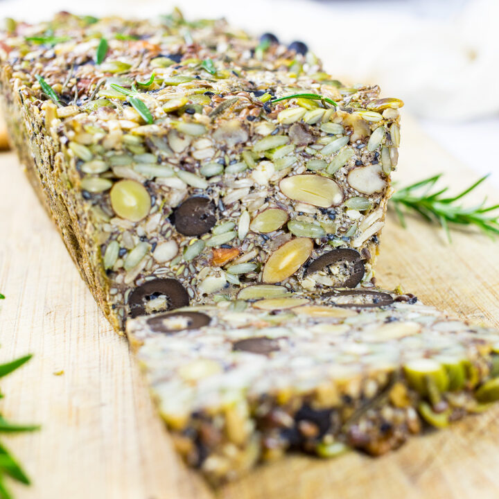 Paleo Nut and Seed Bread Sliced on a chopping board with roasemary in the background.