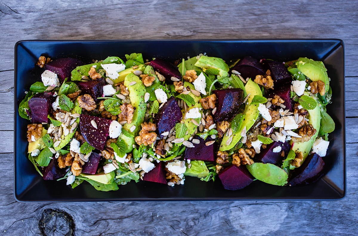 Birdseye view of beetroor, avocado and feta salad on black platter on wooden table.