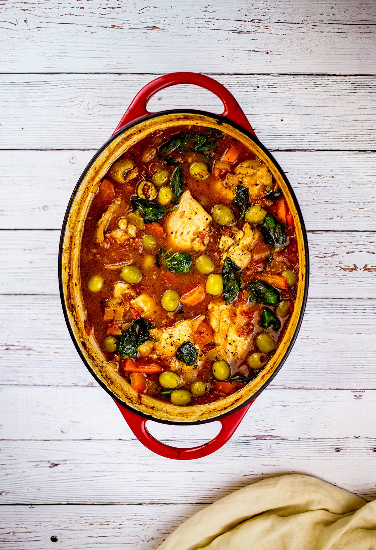 Birdseye view of Spanish chicken stew in red dish on white background.