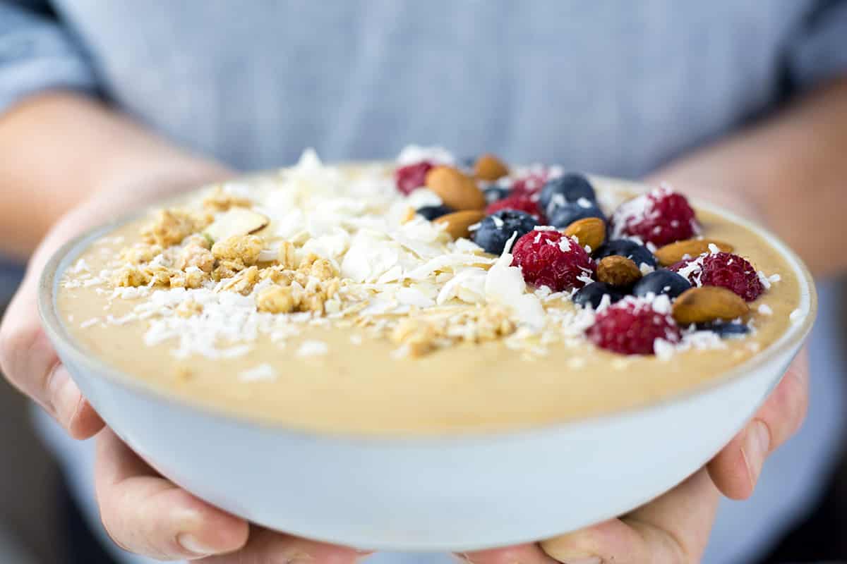 Hands holding peach smoothie bowl.