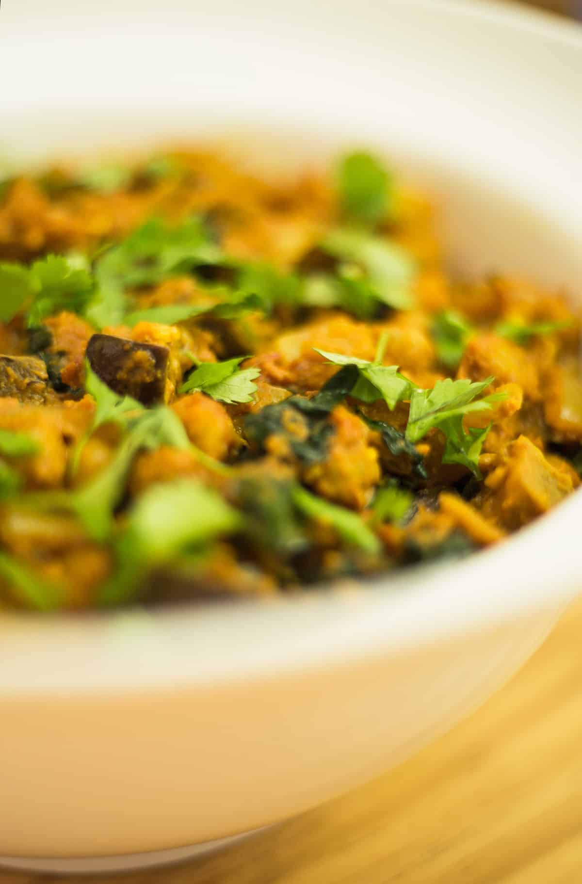 Close up of aubergine and chickpea curry in a white bowl on wooden background.