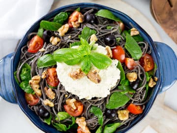 Birdseye view of black bean spaghetti in blue serving dish with wooden servers to the side.