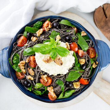 Birdseye view of black bean spaghetti in blue serving dish with wooden servers to the side.