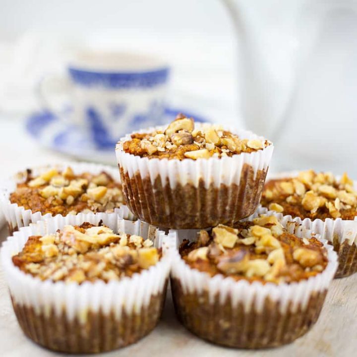 Pumpkin banana muffins on board with teapot and blue and white cup and sauce behind.