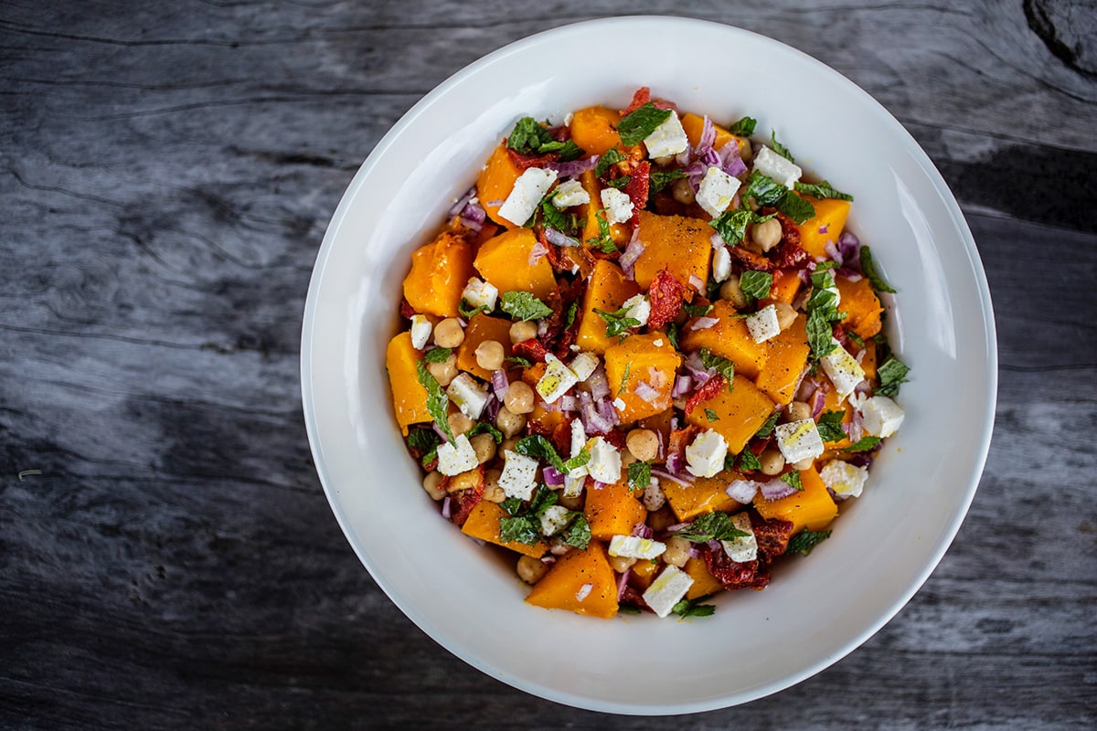 Birdseye view of pumpkin and chickpea salad in white bowl on dark wooden table.