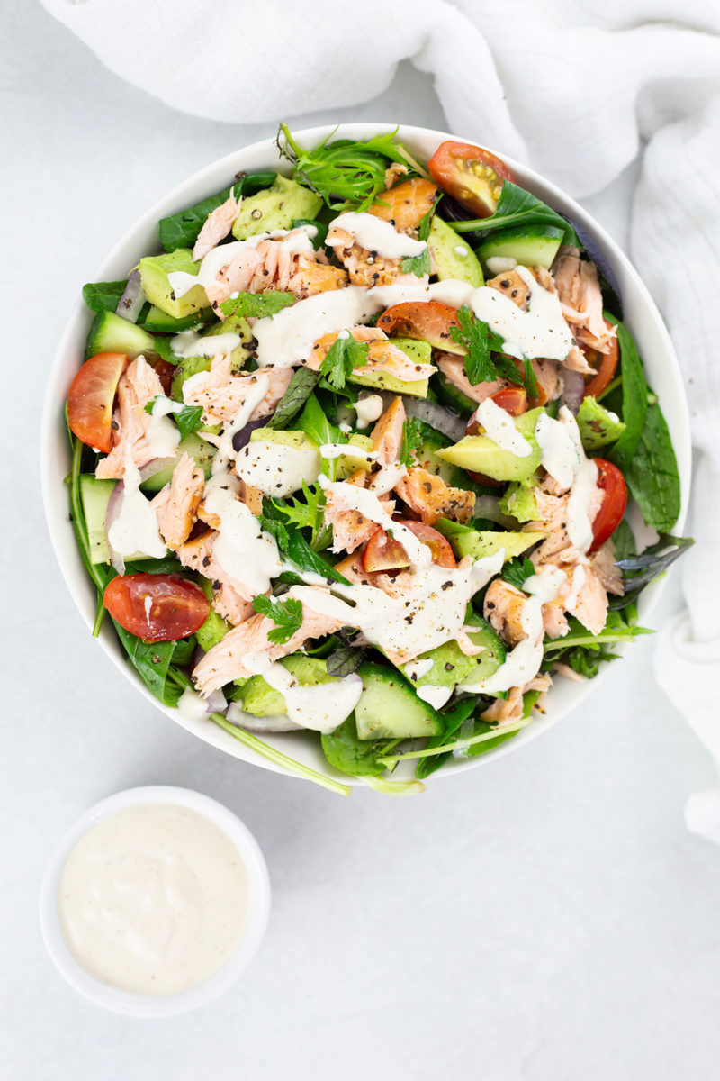 Smoked salmon avocado salad in a bowl with the creamy dressing drizzled over the top.