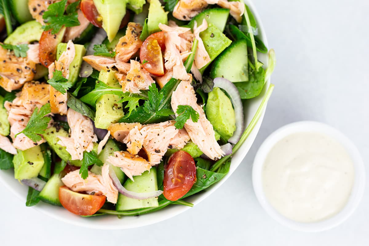 Smoked salmon avocado salad in white bowl with small bowl of lemon cashew dressing to the right.