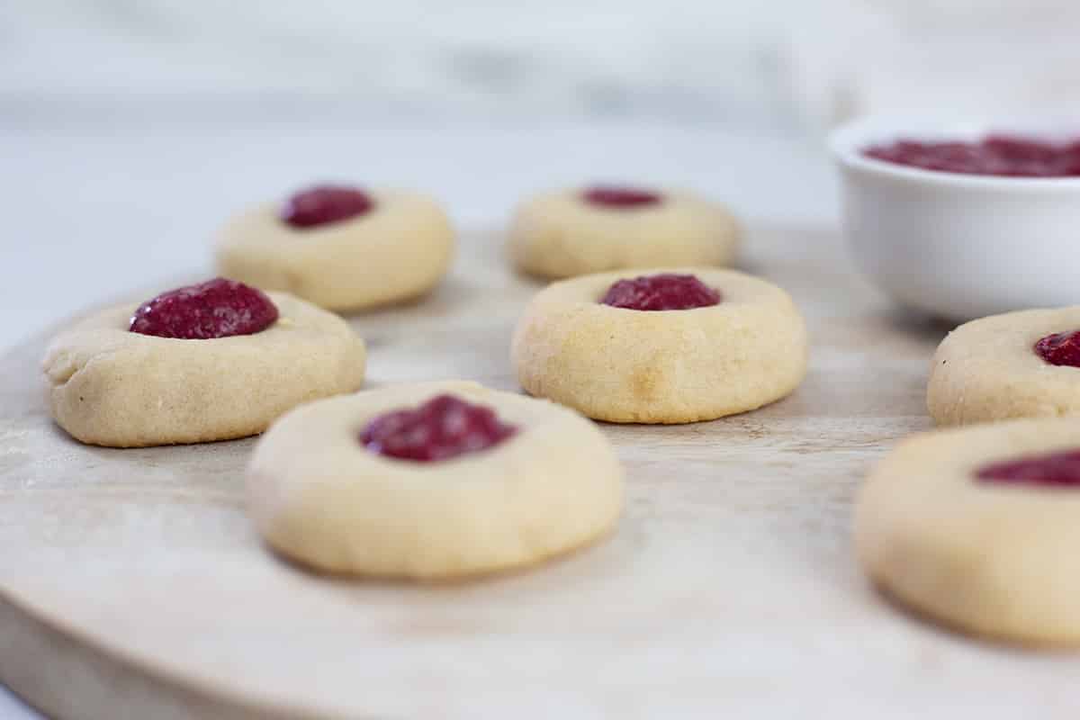 Thumprint coookies on board with pot of chia jam behind.