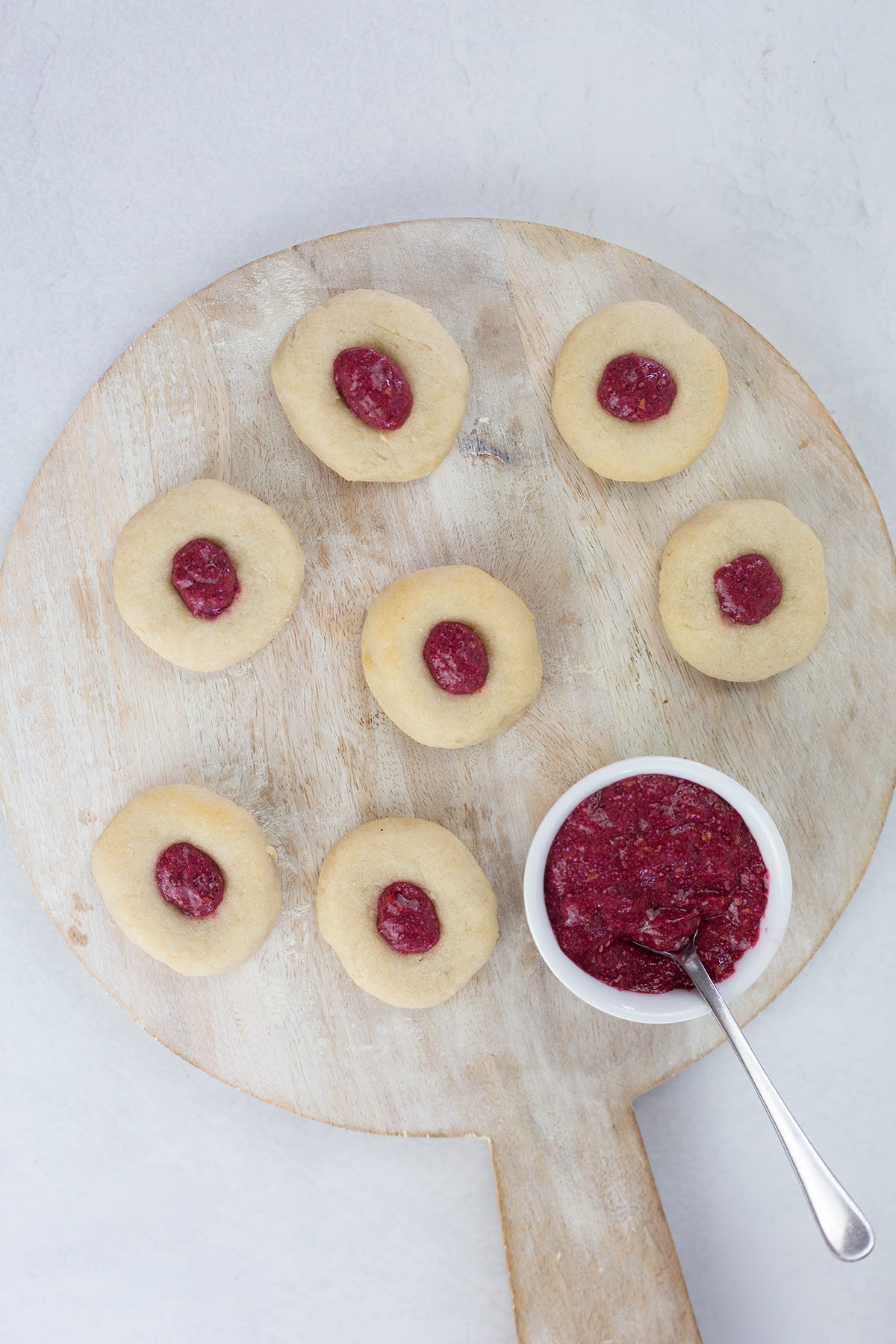 Birdseye view of thumprint cookies with small white ball with raspberry chia jam and tea spoon.