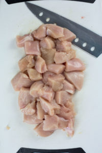 Diced chicken on board with knife for Greek chicken bowl