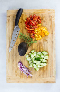 Prepper vegetables for greek salad bwol on wooden board with knife.