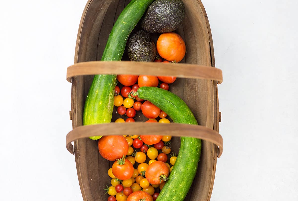 Tomatoes, cucucmber and avocado in wooden basket.