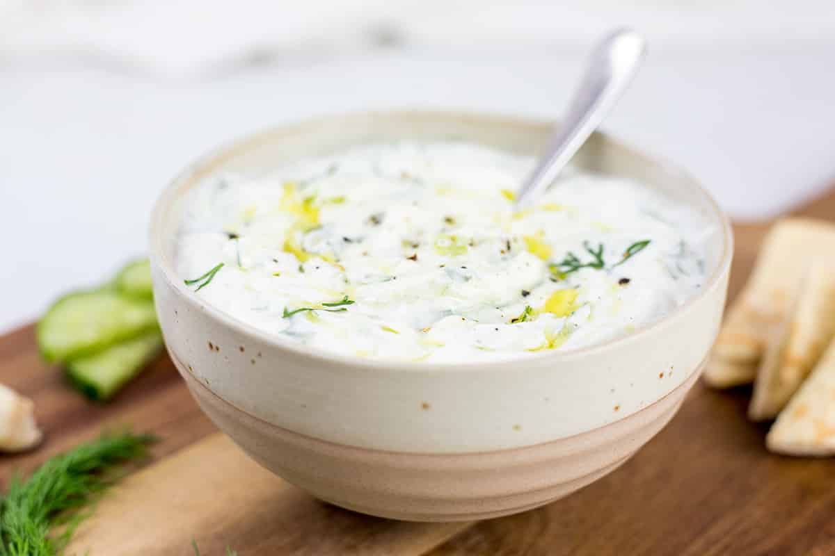 Close up of creamy dairy-free tzatziki in brown and white bowl with spoon in.