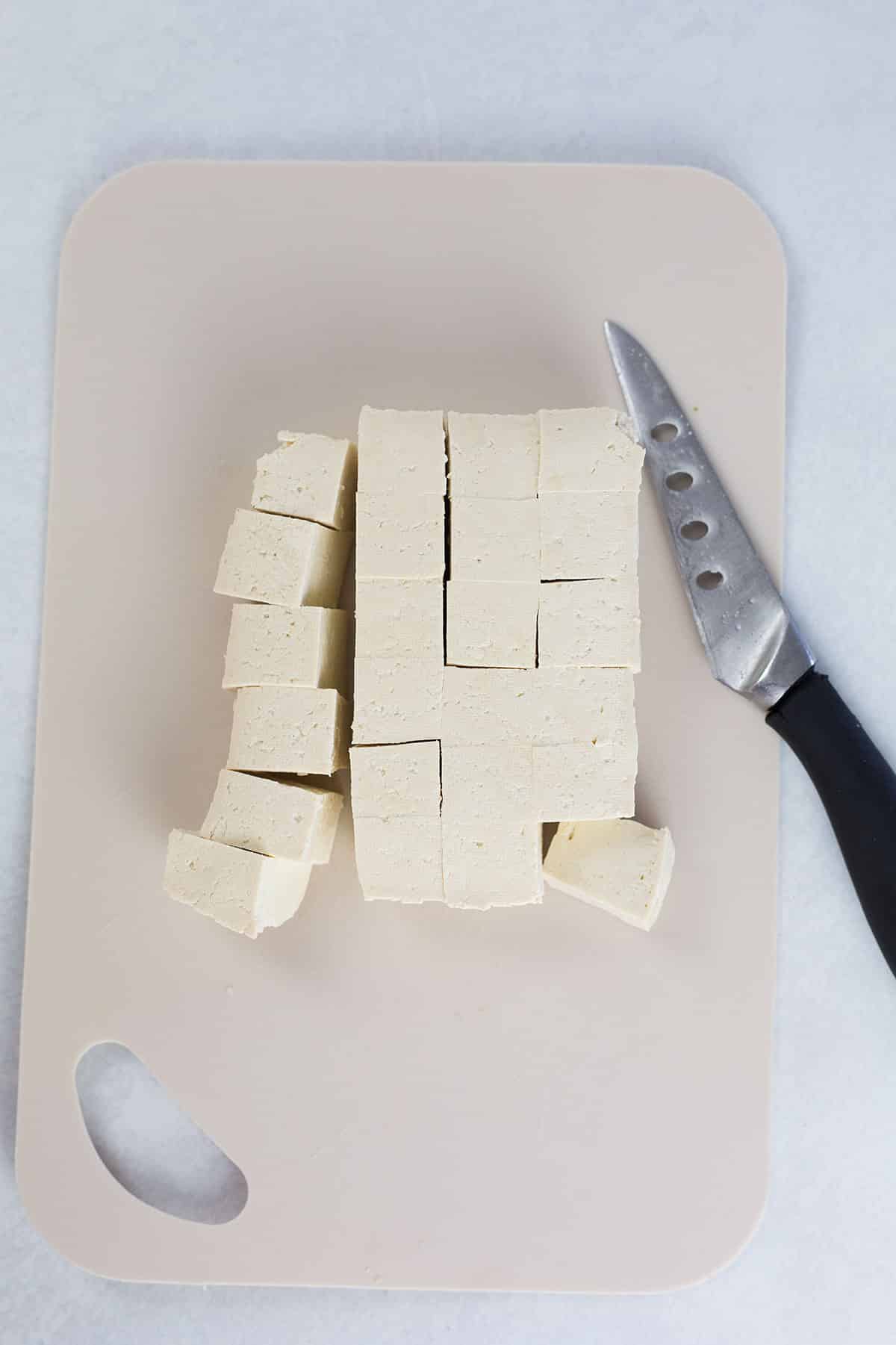 Tofu sliced on board with knife to the side.