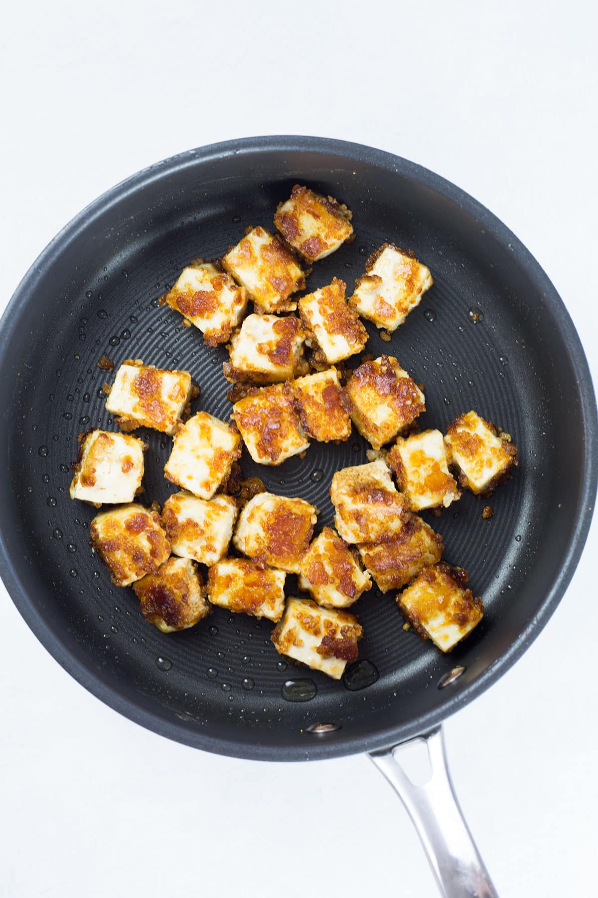 Tofu being cooked in black pan.