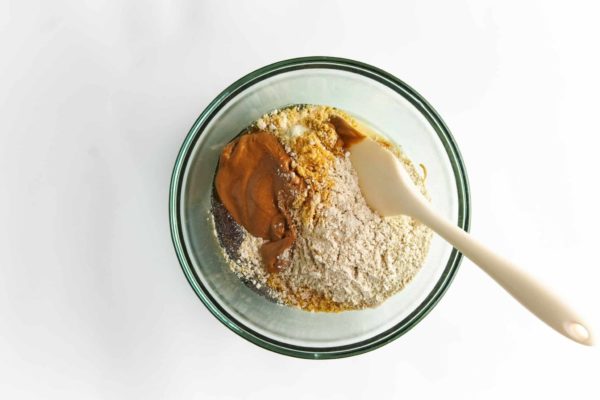 Stirring peanut butter and other ingredients in glass bowl with wooden spoon.