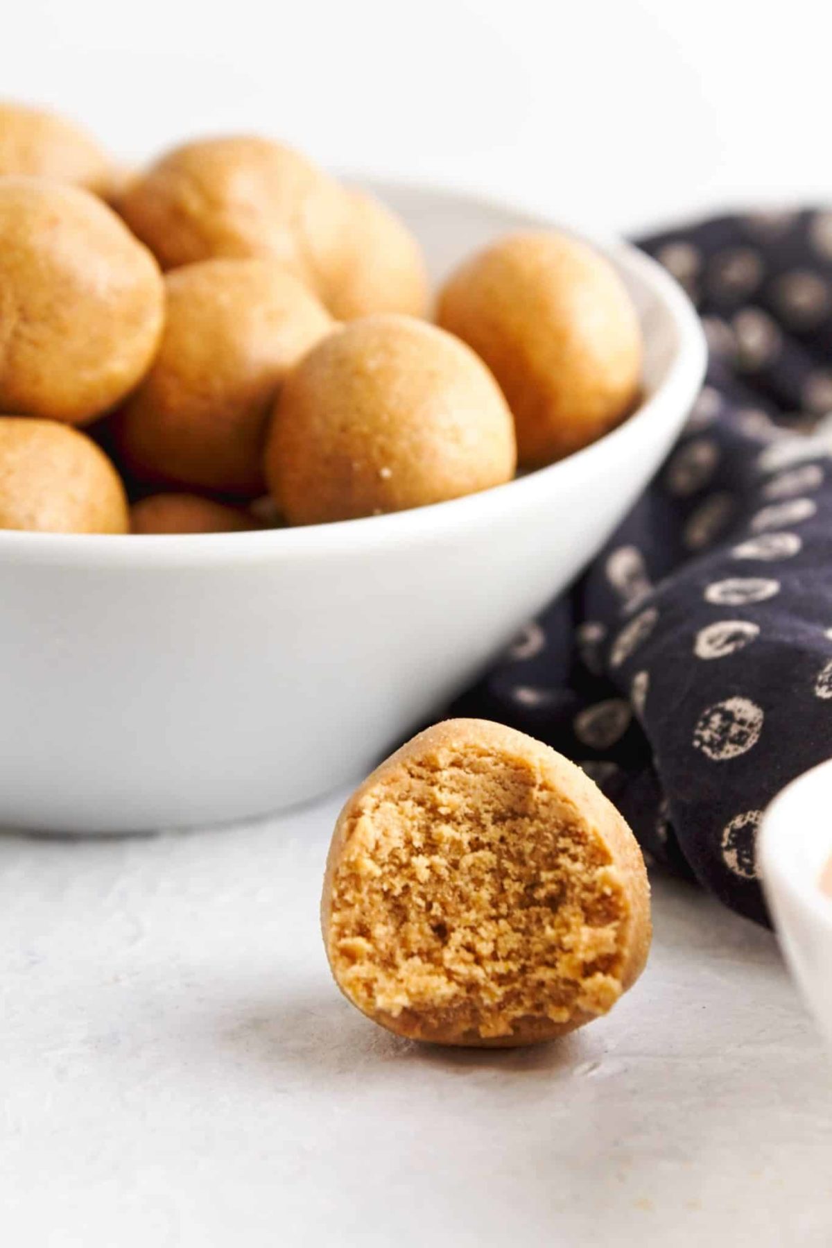Bowl of peanut butteer protein balls with one half bitten on its own in front of bowl on white background.