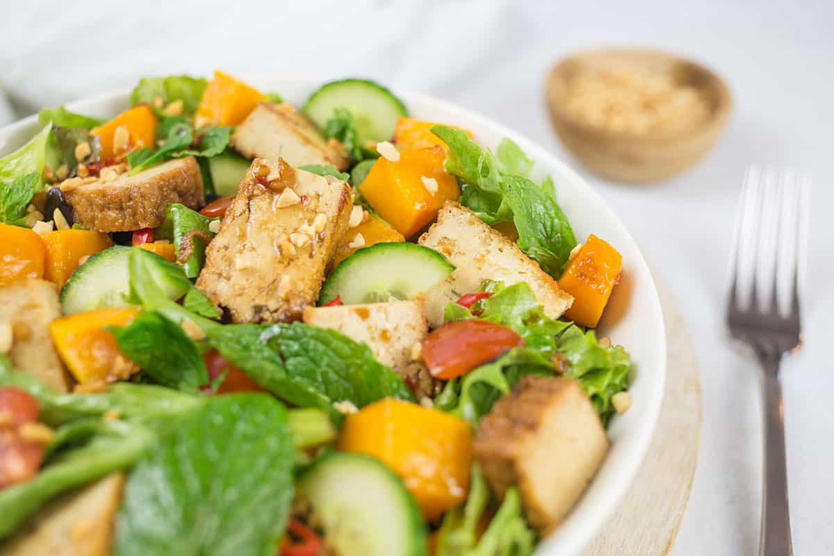 Close up of tofu pumpkin salad with fork and peanuts behind.
