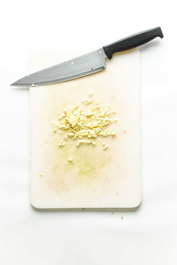 Chopped garlic on white board showing knife for chimichurri