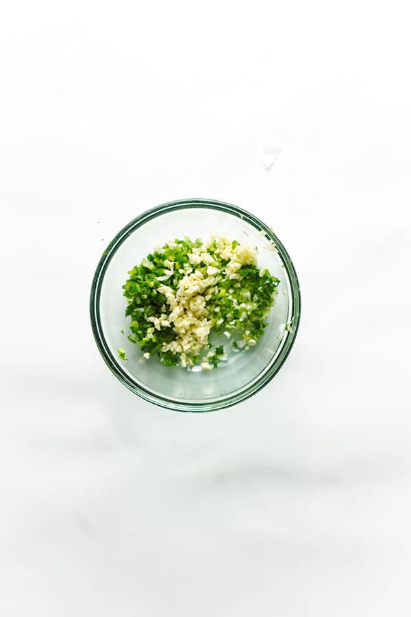 Chopped ingredients in glass bowl for chimichurri.