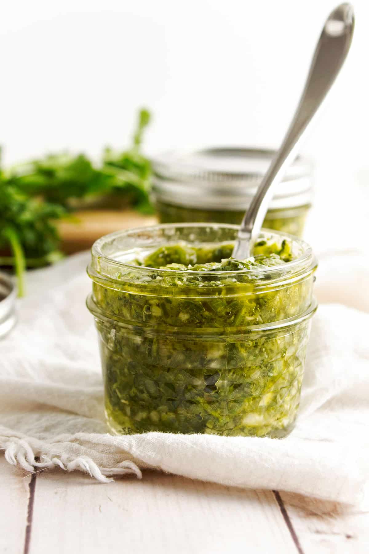 Coriander chimichurri in glass jar with spoon sticking out.