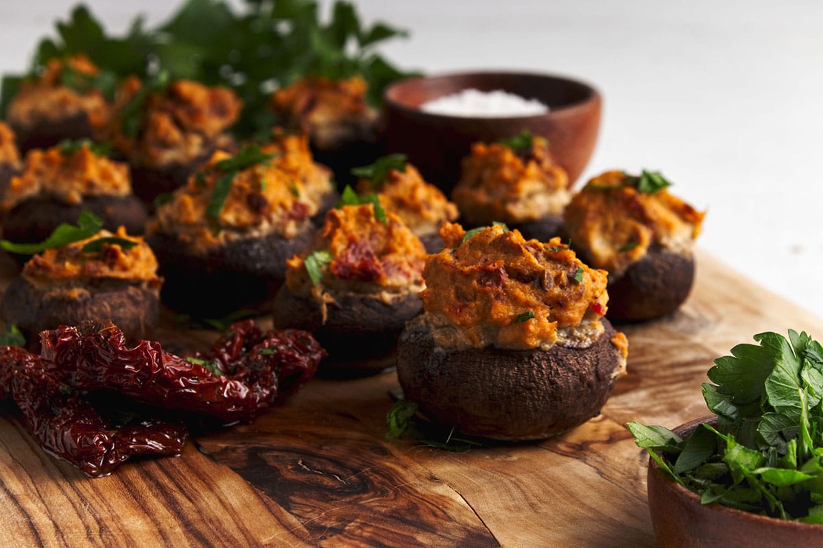 Close up of Vegan stuffed mushrooms on serving boards with bowl of parsely in front.