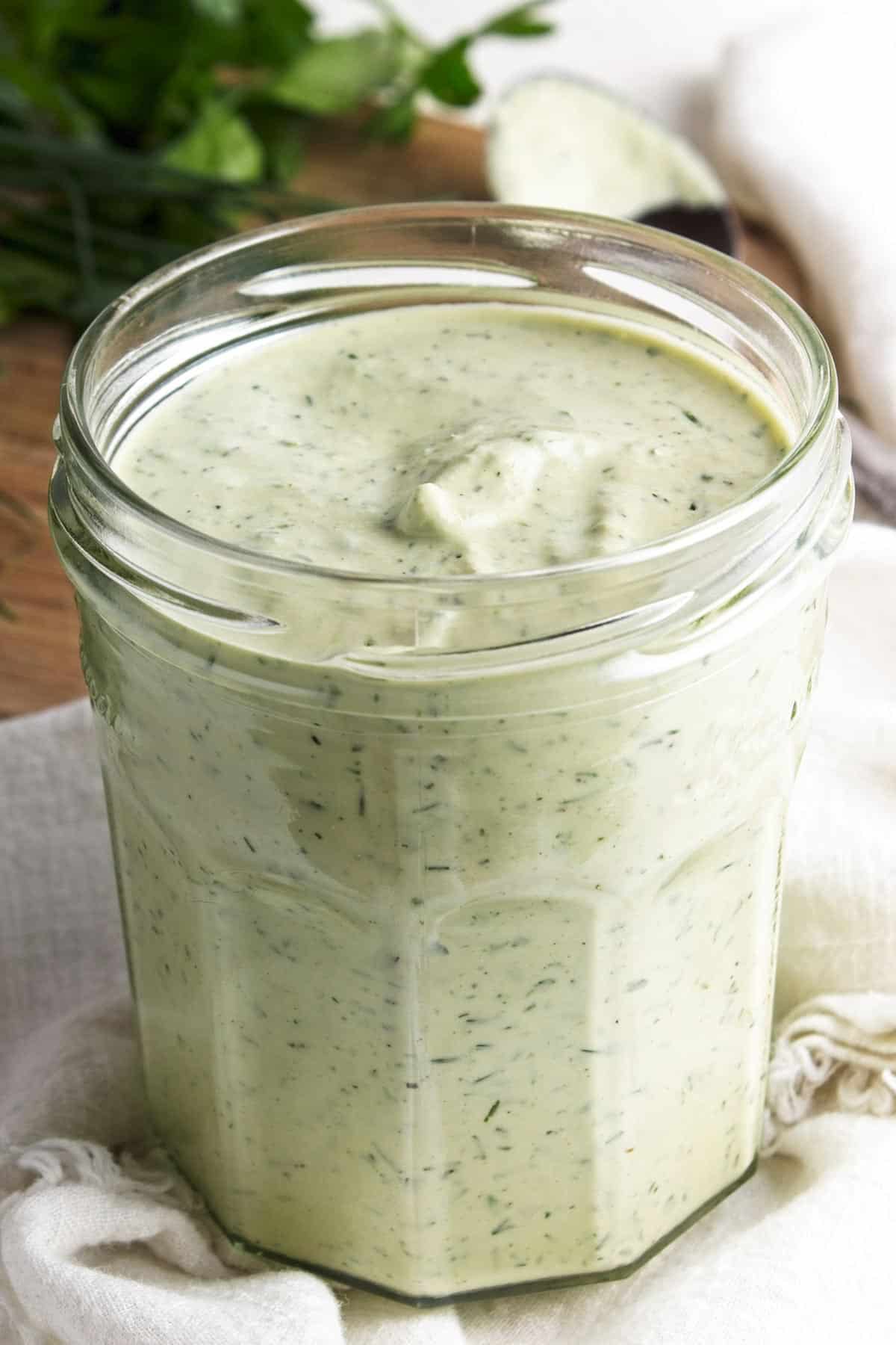 Close up of jar of dairy-free ranch dressing in jar on white cloth.