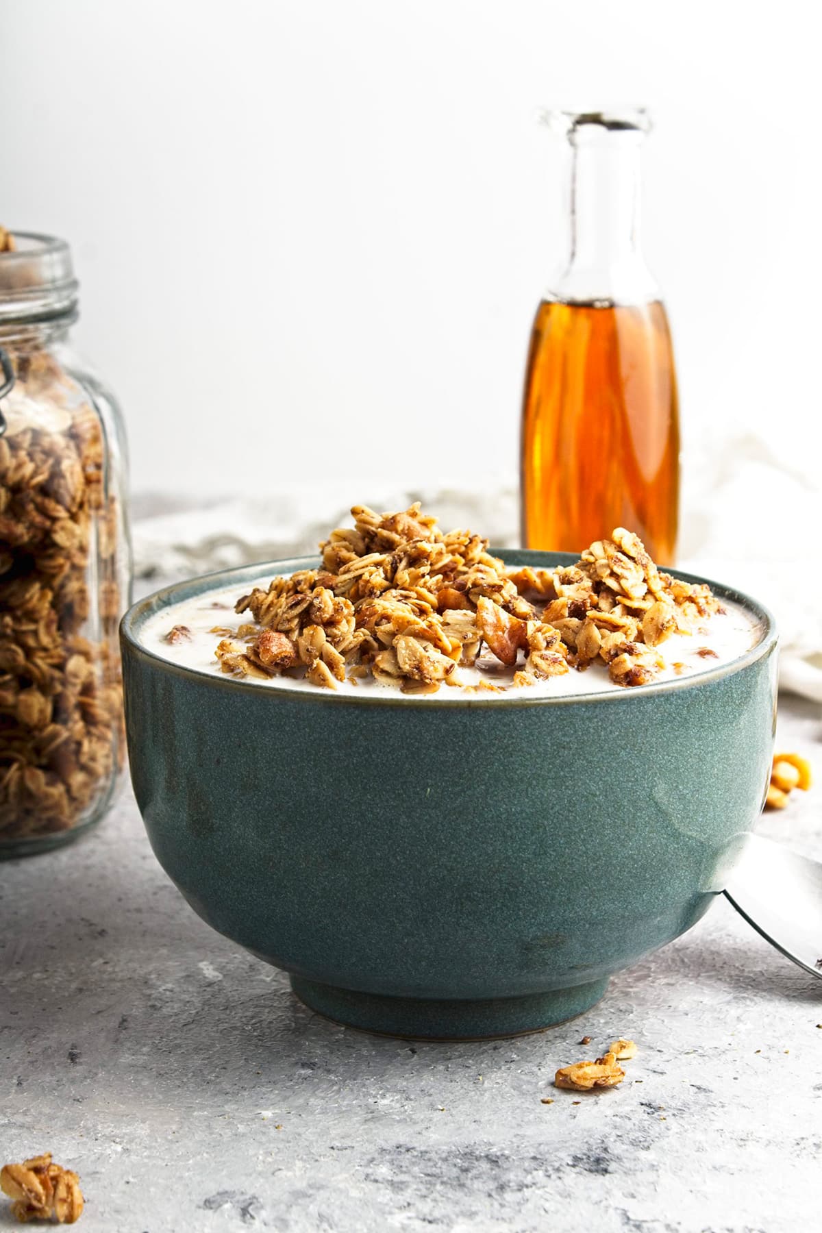 Granola in bowl with maple syrup and jar of granola in background.
