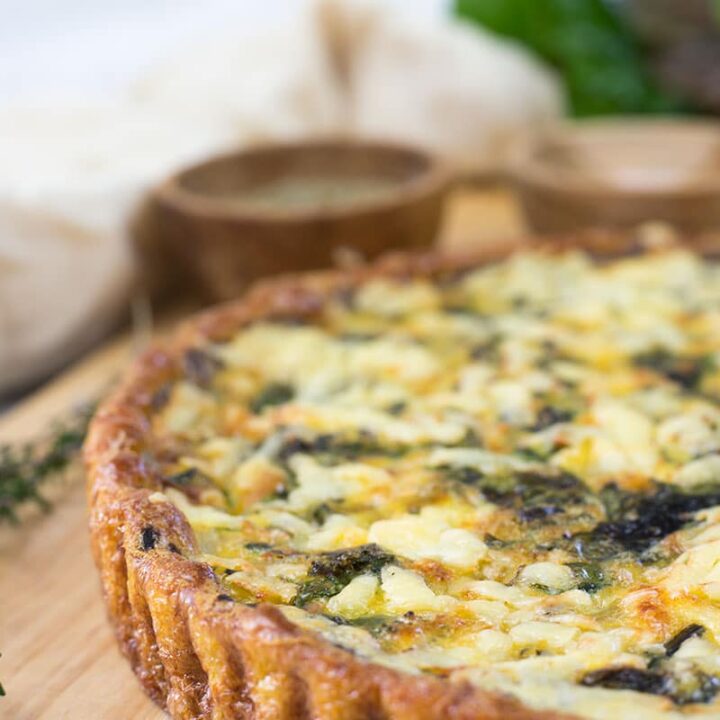 Quinoa quiche on board, with salt and herbs in the background.