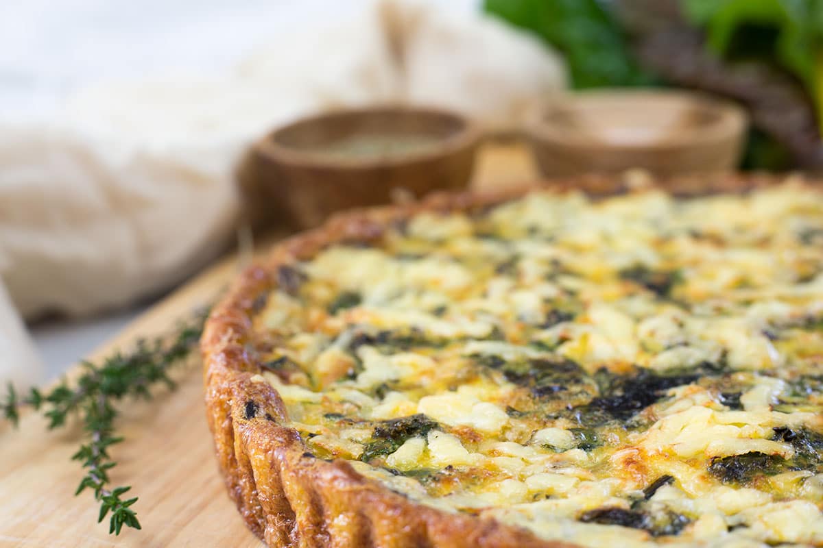 Quinoa quiche on board, with salt and herbs in the background. 