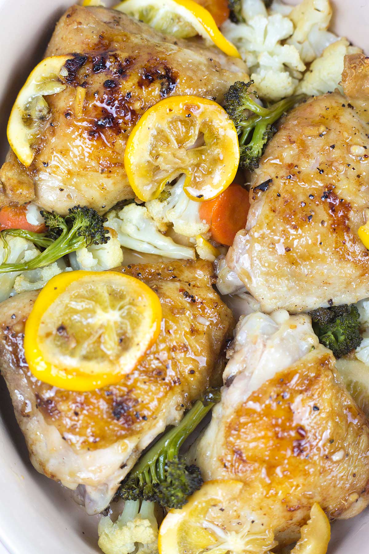 Close up of honey lemon pepper chicken thighs and lemon wedges and vegetables in dish.