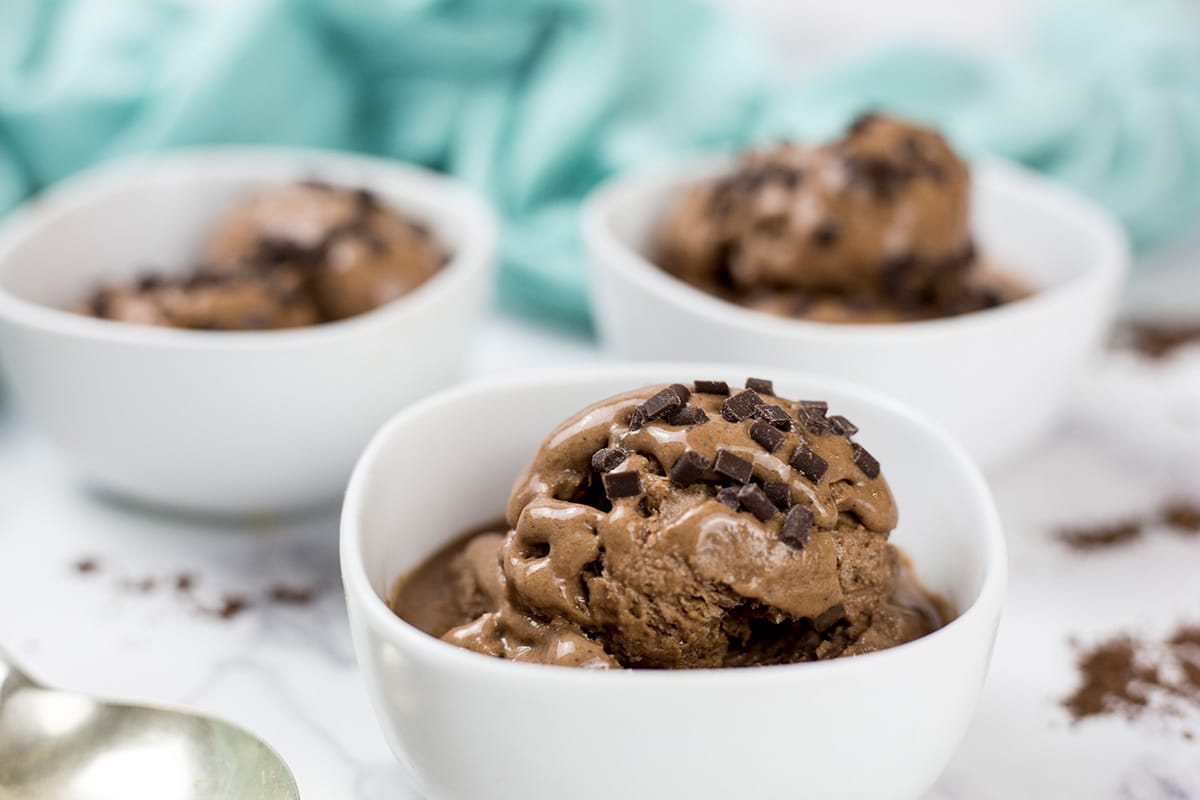 Close up of 3 bowls of chocolate banana nice cream with green cloth behind. 