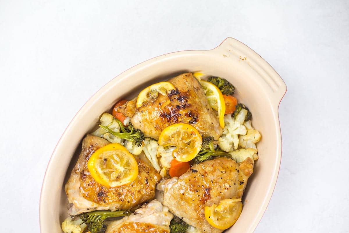 Lemon pepper chicken thighs in casserole dish with veggies and lemon slices.