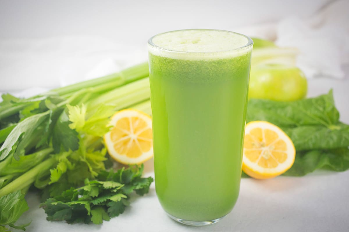 Green juice with vegetables and lemon behind.