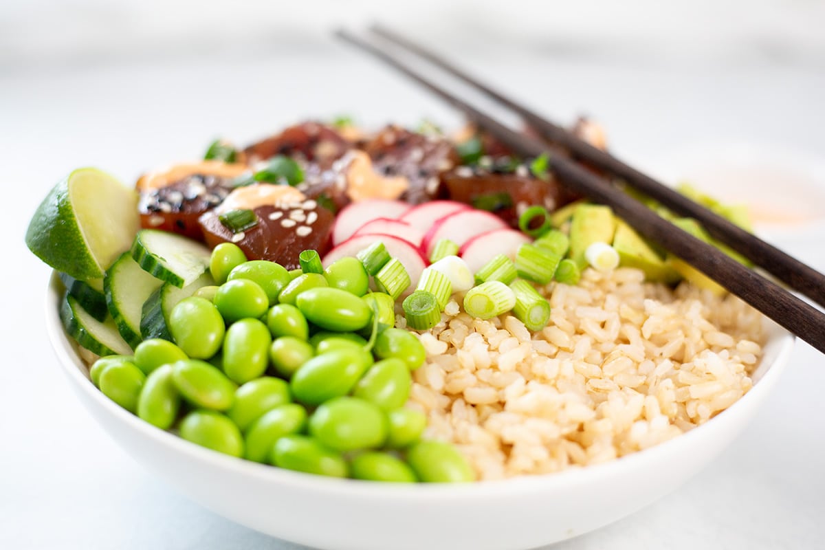Close up of spicy tuna poke bowl in white bowl with brown chopsticks over the top.