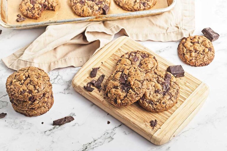 Buckwheat chocolate chip cookies on board, tray and pile of cookies to the left.