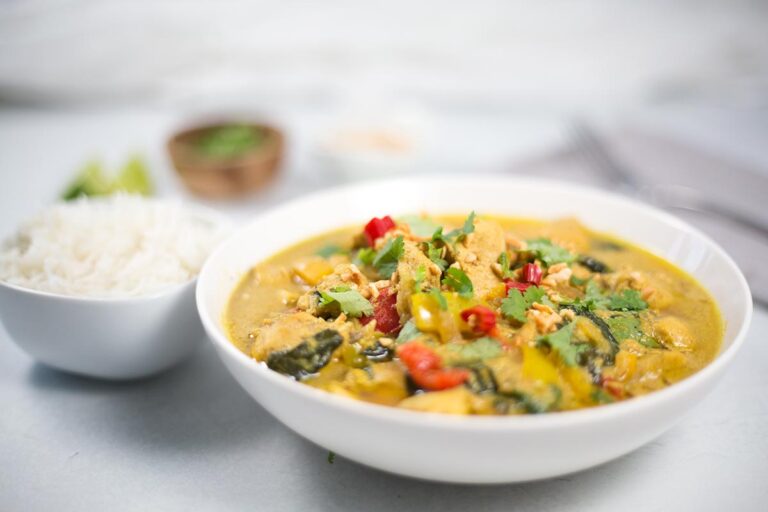 Slow Cooker Chicken satay in white bowl with rice and coriander behind.